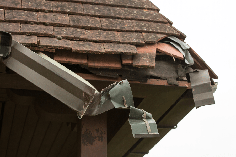 A broken corner and downspout while the shingles are also falling off.