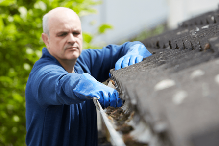 A homeowner considering gutter cleaning costs while on his roof.